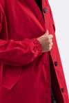 A person wearing The WJacket's Water Resistant Oversized Hooded Windbreaker Rain Jacket, featuring black buttons, is shown in this image. The individual's right hand is adjusting the collar or front of the coat, showcasing its timeless style. The image focuses on the upper torso and part of the arm.