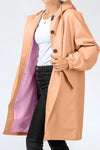 A person wearing a stylish, peach-colored looselyboho PEACH FUZZ WINDBREAKER with black buttons draped open to reveal a light purple lining. The lightweight water-resistant material keeps them dry while their white shirt and black pants add a touch of elegance. The person's face is out of frame.