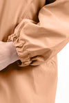 Close-up image of a person wearing the looselyboho PEACH FUZZ WINDBREAKER in a beige shade. The focus is on their sleeve, which is gathered at the wrist with elastic, creating a puffed effect. Made from lightweight water-resistant material, the person's hand is slightly visible as they adjust the sleeve with their other hand.